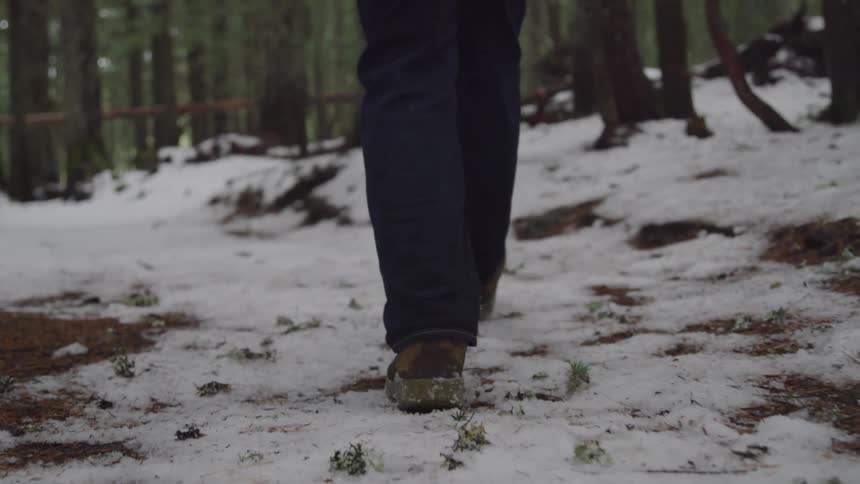 Man with pants and boots walks on a dirt track in snowy forest