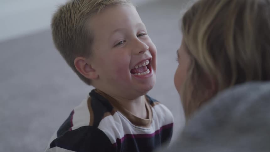 A child laughs as a woman plays with him