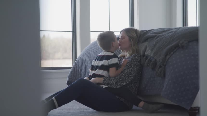 Boy kisses mother as they sit on floor near bed