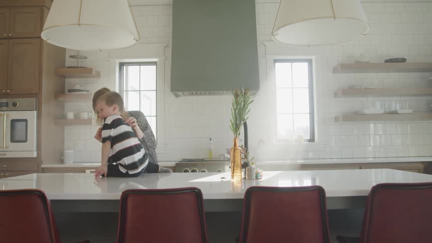 A mother and young son play together in the home kitchen