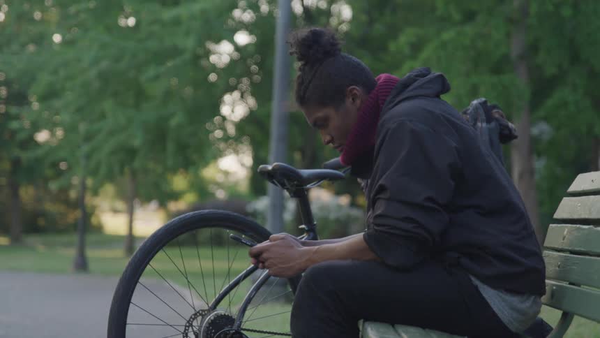 A man sits on a park bench on his cell phone with a bicycle beside him