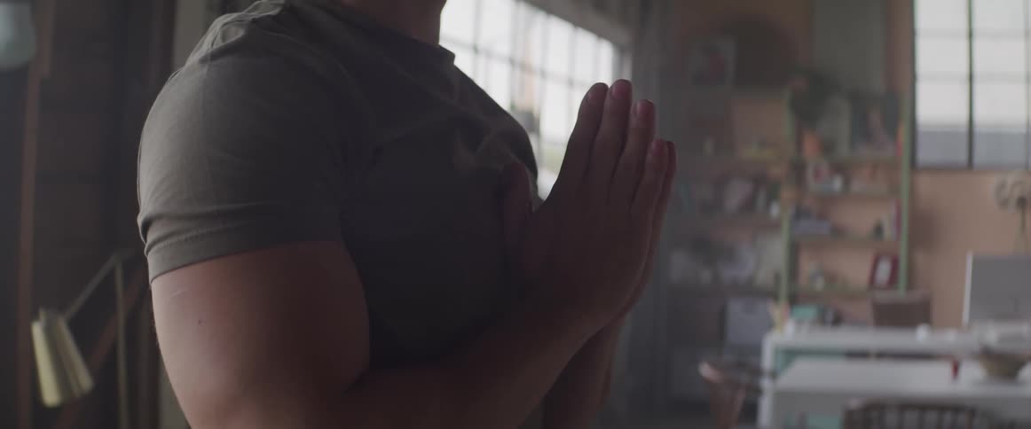 Young muscular man holds hands in prayer in a room at home