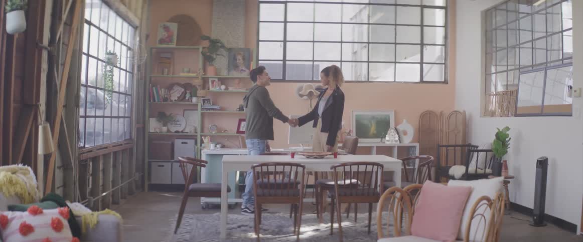 A man and woman shake hands while standing in an apartment kitchen