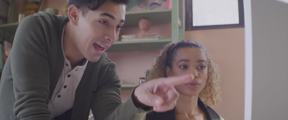 A man and woman look at a computer screen and the man points and talks to the woman