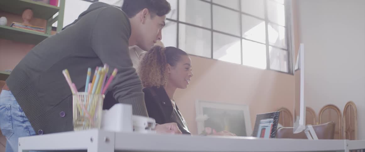 Man and woman discuss contents they are viewing on computer monitor in brightly lit office