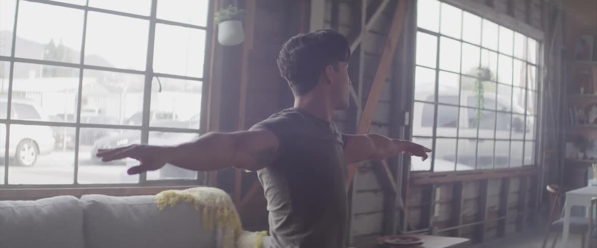 A man holds his arms outstretched as he practices yoga indoors