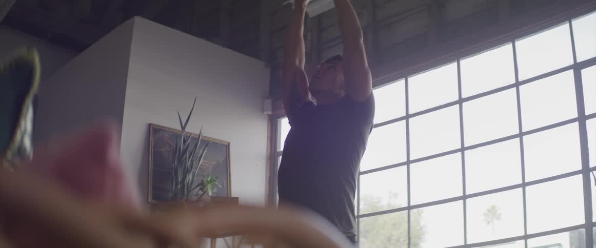 A young man does yoga in front of a large window in a house during the day