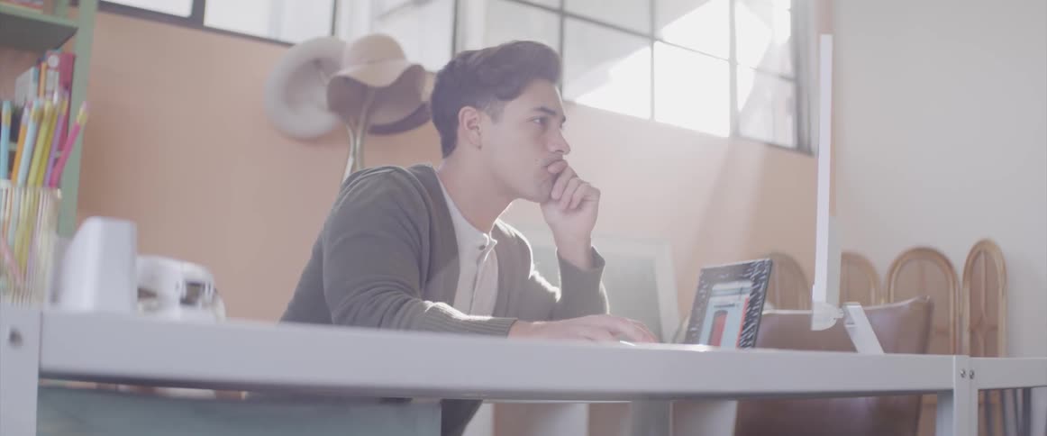 A man sits at a desk looking at a large computer monitor
