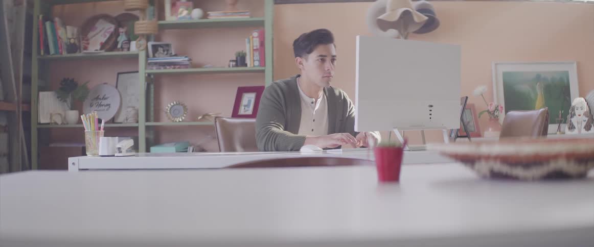 A man sits at a desk in front of a computer with large monitor