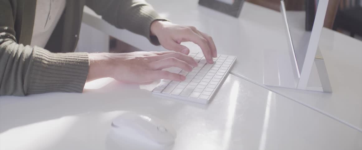 Man sitting at a white desk uses a computer and types on a keyboard in an office