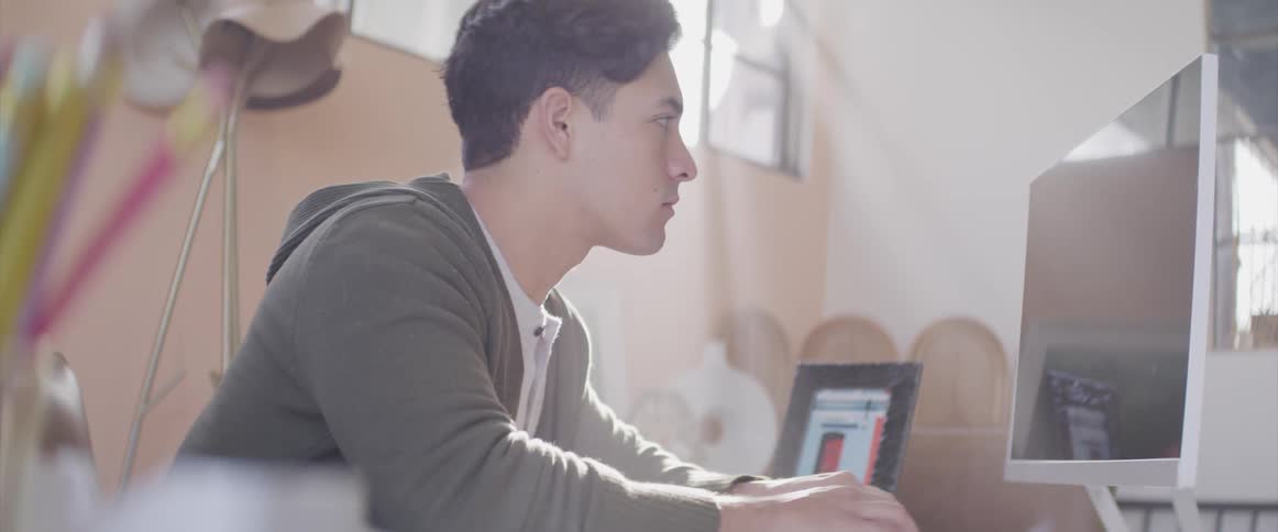 A teenage boy sits at home and works on a computer
