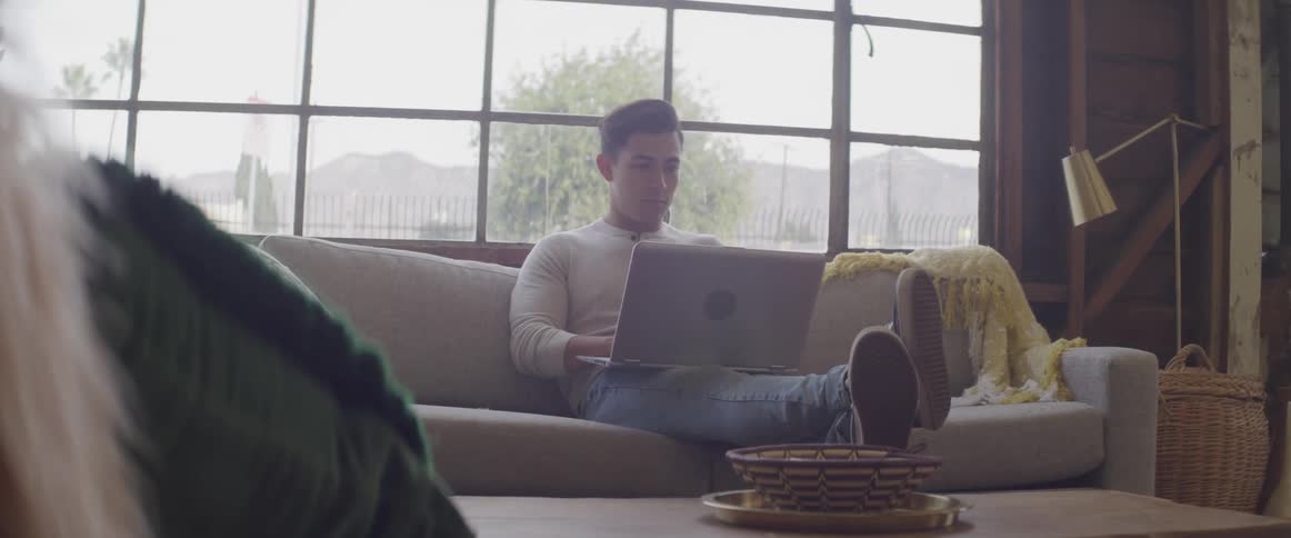 A man sitting on a couch with his feet on a table with a laptop on his lap