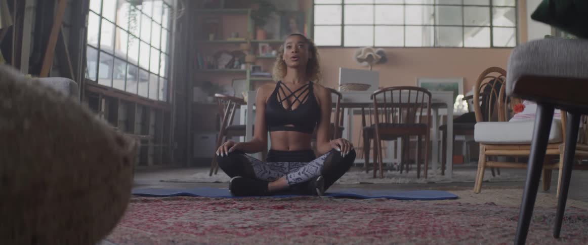 A woman sits on her living room floor in a crossed legged meditation pose