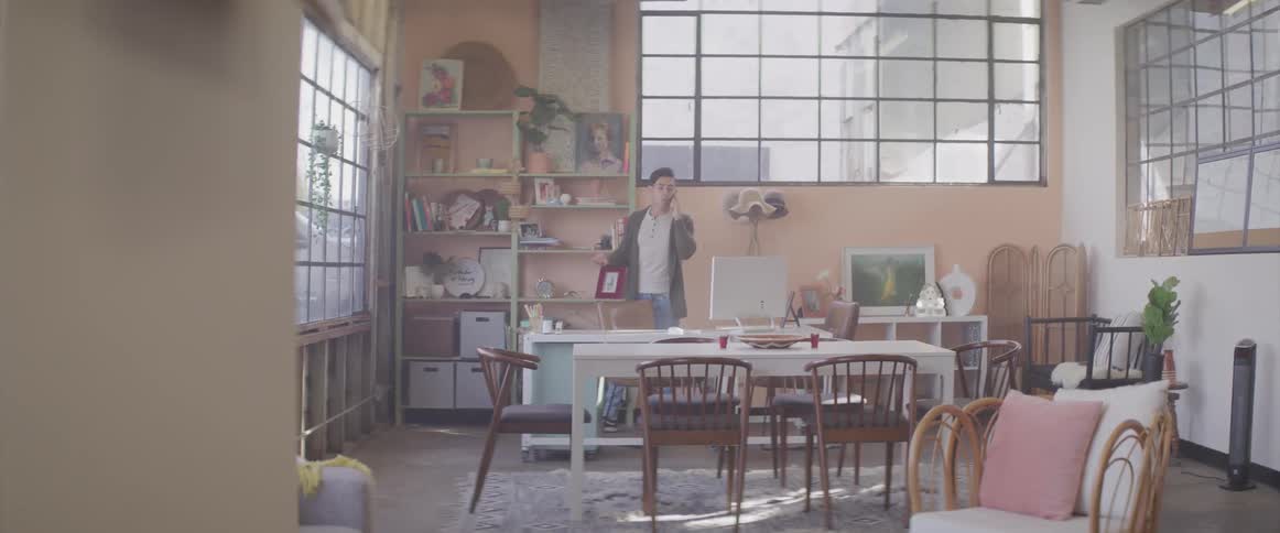 A man walks around a room talking on a cell phone