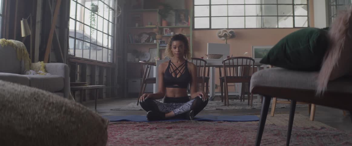 A young woman sits on a yoga mat on the floor with her legs crossed