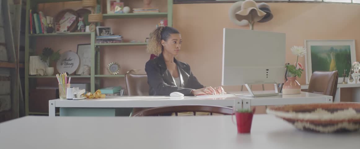 Woman sits at desk typing on keyboard backed by shelves