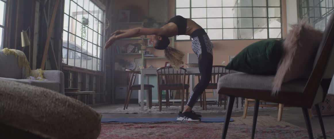A woman does a back bend while doing yoga in her living room
