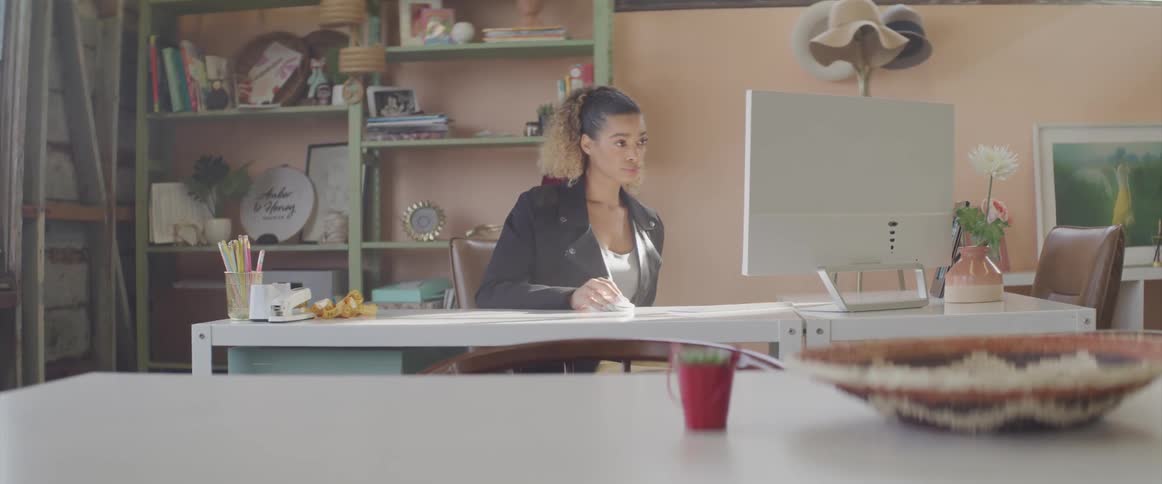 A woman sits at a computer desk in front of a large monitor
