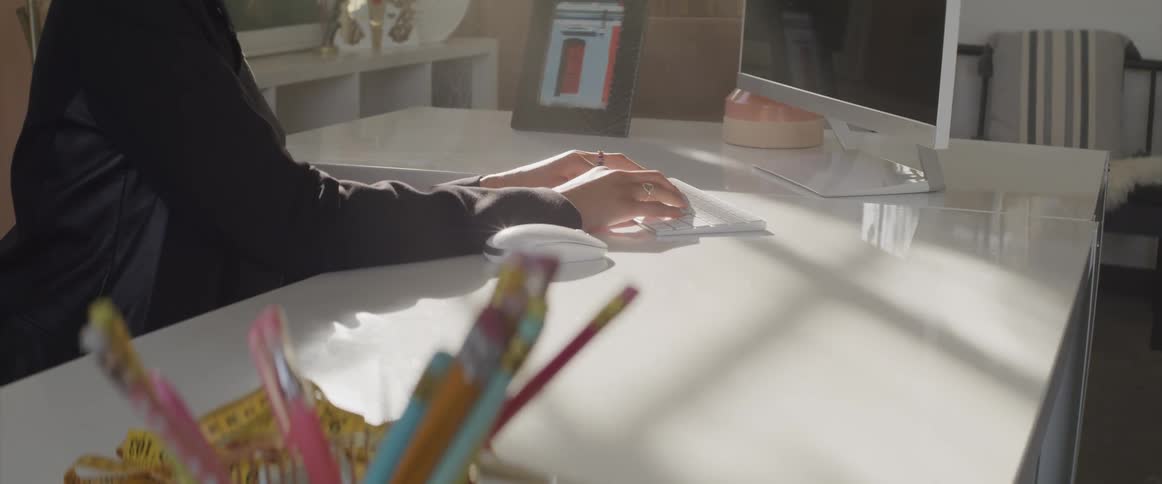 Female sitting at l shaped desk in front of a computer monitor leans forward as she types on the keyboard