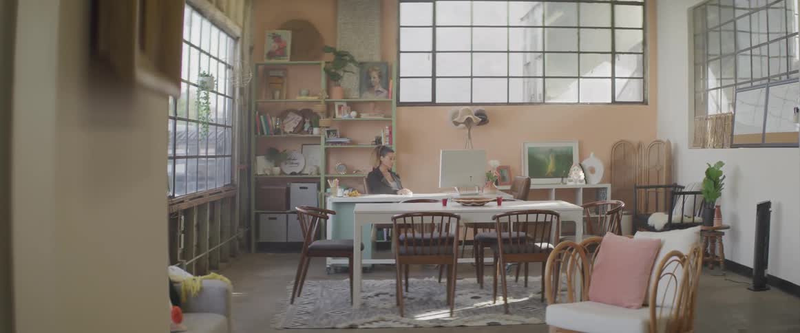 Woman sits at desk using mouse in room with large windows