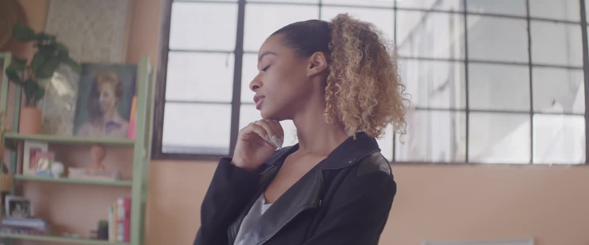 A young woman at home puts her chin in her hand and thinks