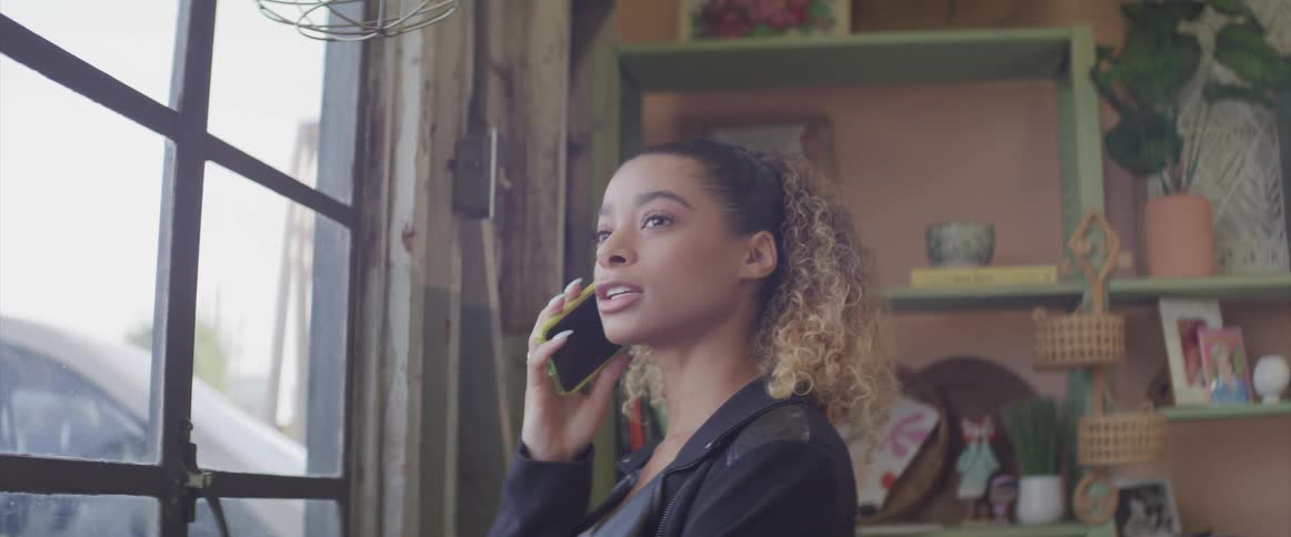 Woman standing near a window in a room talks on her smartphone