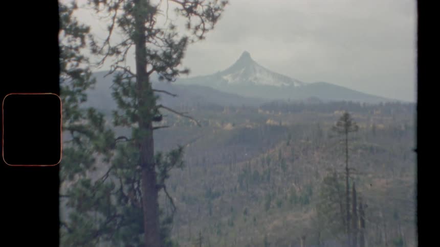 Zoom into a mountain peak in the distance over the forest caught on film