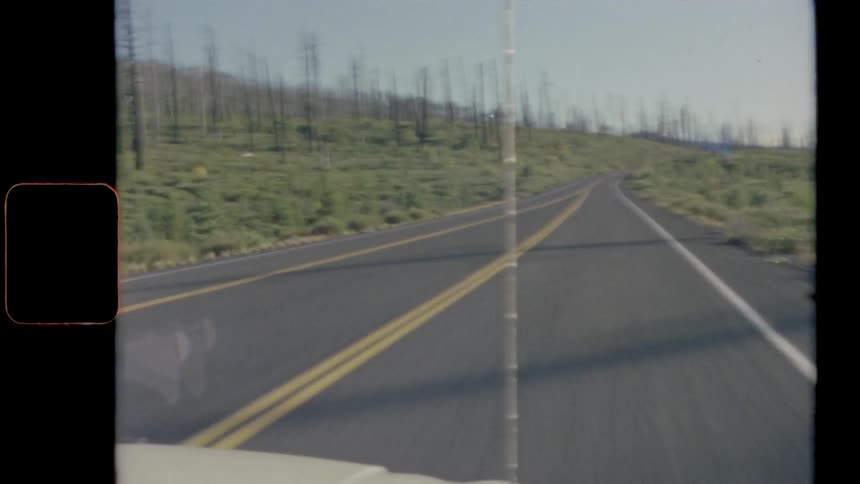 A vehicle driving on a road with trees grass and the sky in the background
