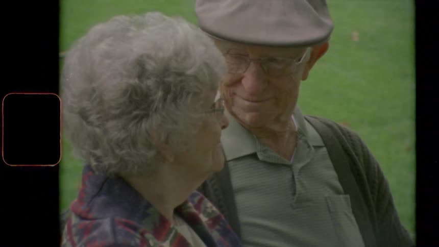 Elderly couple sitting in a bench in the park look at each other lovingly