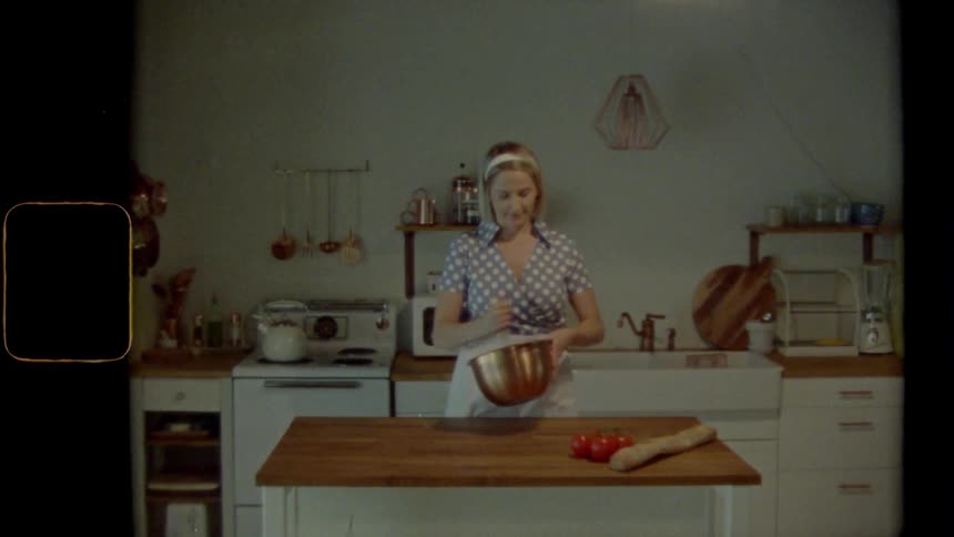 Woman stands behind island in kitchen mixing contents of bowl quickly