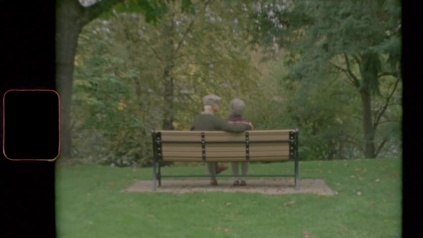 An elderly man and woman sit on a park bench together