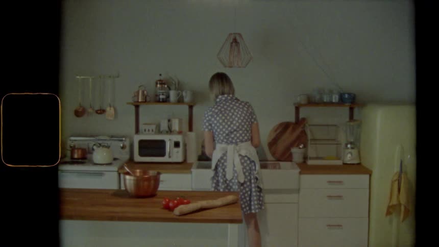Blonde woman wearing apron stands washing at kitchen sink