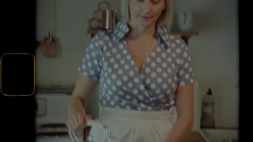 A woman pours a liquid from a kettle into a cup and smiles into the camera as the camera pans upward