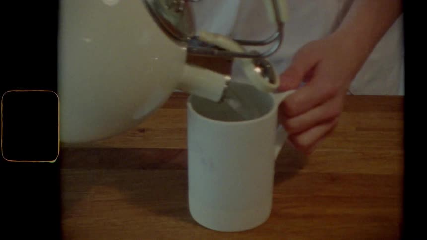 Vintage footage of a woman pouring water from a kettle in a to a mug