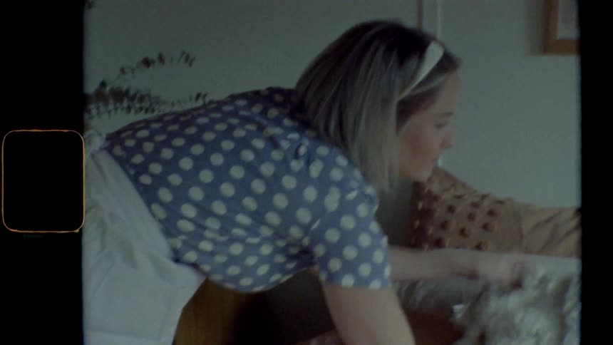 Blonde housewife with a blue dress makes the bed in bedroom