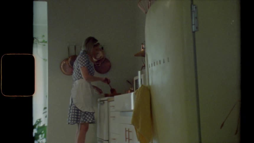 Woman stands at stove in predominantly white colored kitchen stirring food in skillet