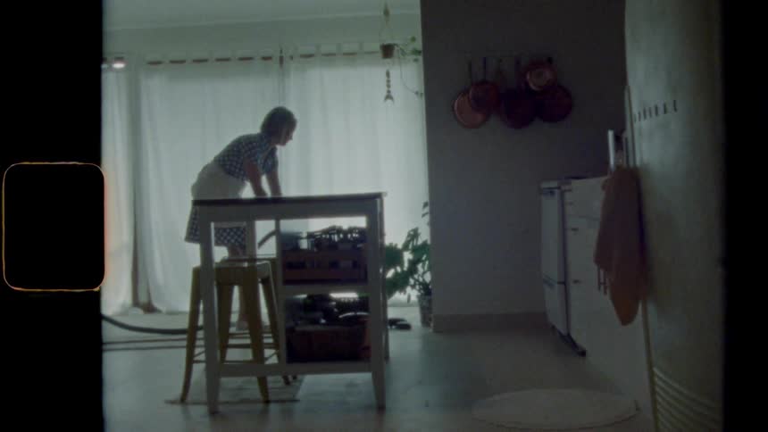 A woman in an apron vacuums a home kitchen floor