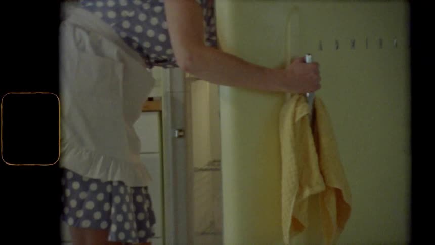 A woman walks to her fridge and gets something out of it