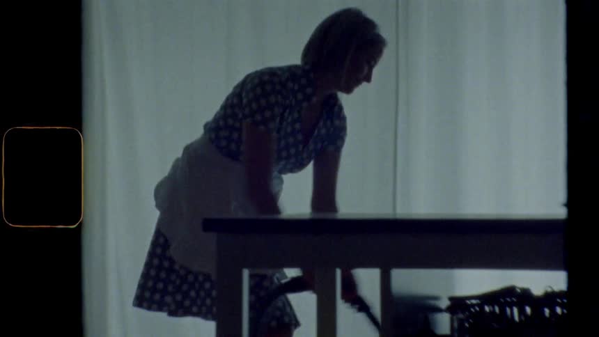 Blonde woman wearing apron vacuums the floor using a canister vacuum