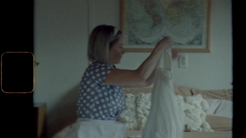 Blonde housewife sits on bed and folds the laundry in bedroom