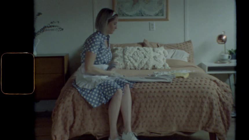 A woman in a bedroom sitting on a bed and folding a piece of clothing