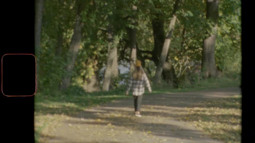 A woman walks along a path in a park as yellow leaves fall from the trees beside the path
