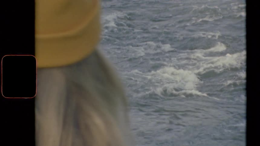 A person with a hat in front of the ocean with waves and ripples in the water