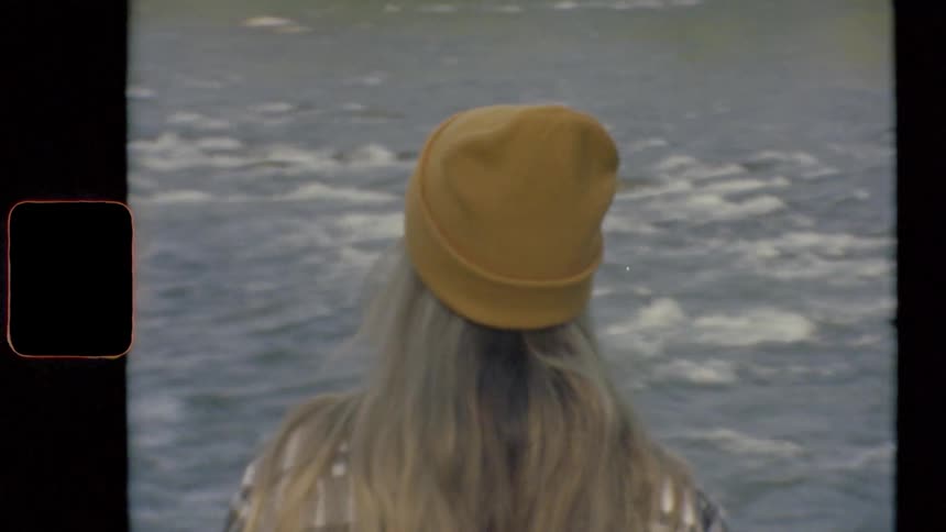 A woman with a hat standing by a river with water flowing