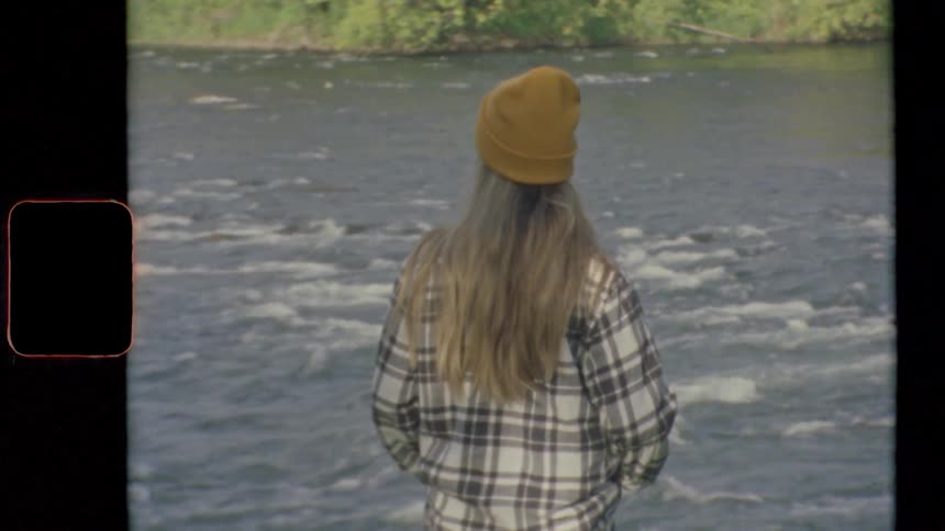 A woman with a hat standing by a river with flowing water