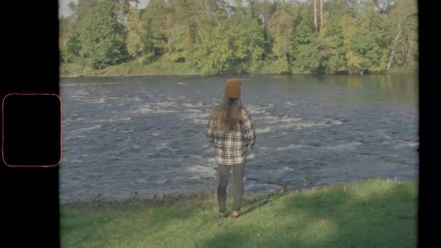 A young woman stands along the side of a fast flowing river