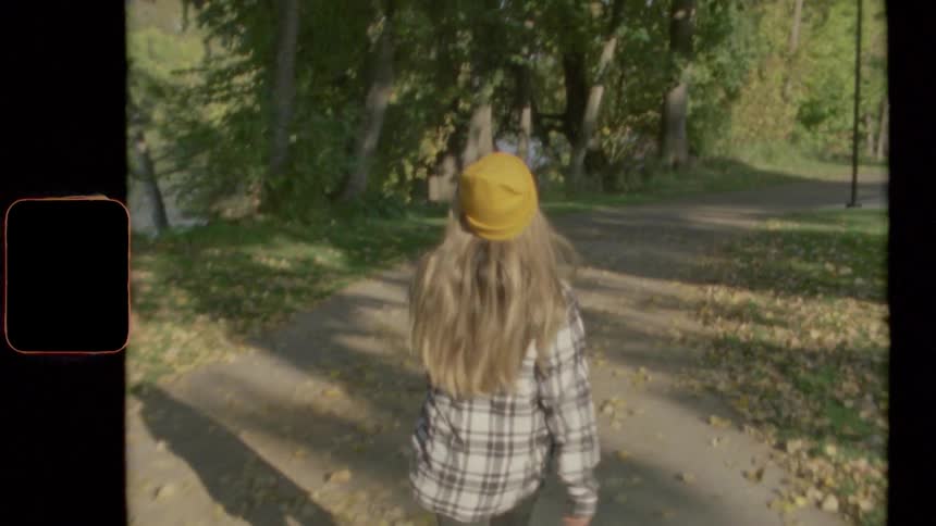 Girl wearing yellow beanie and flannel shirt walking along pathway near a lake