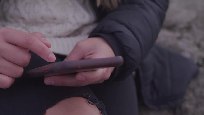 Woman with ripped jeans and a white sweater uses a smartphone