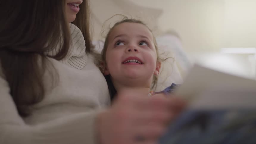 A mother sits in bed with her daughter and reads to her