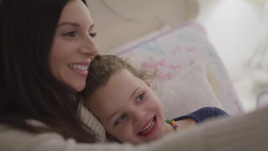 A mother sits in bed with her daughter and they talk and laugh